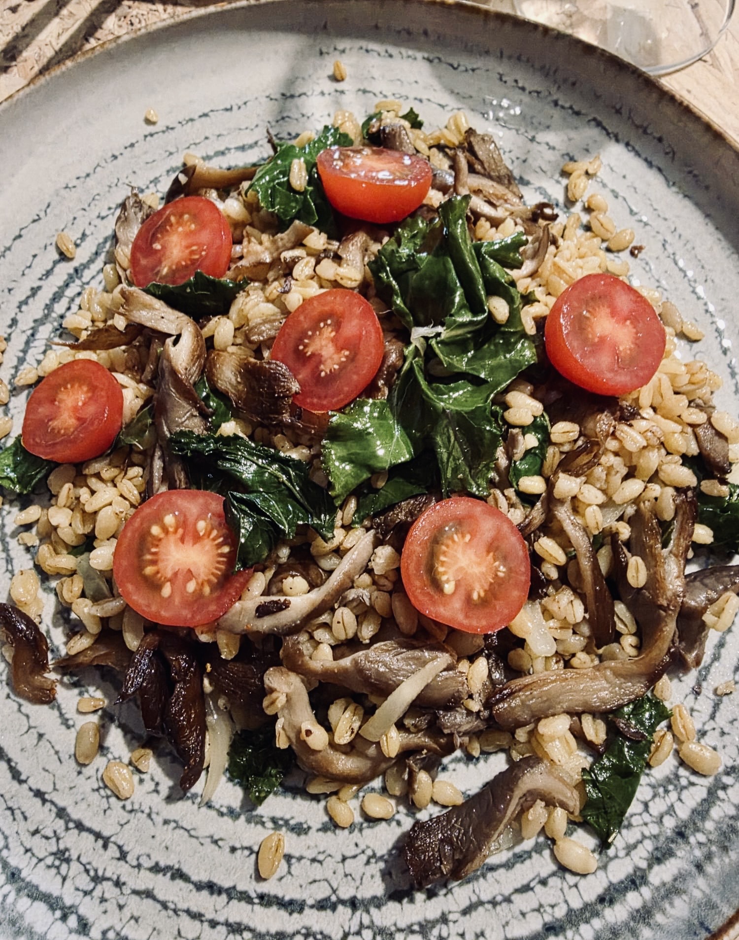 Bol de blé garni de pleurotes sautés, feuilles de chou kale et tomates cerises coupées.