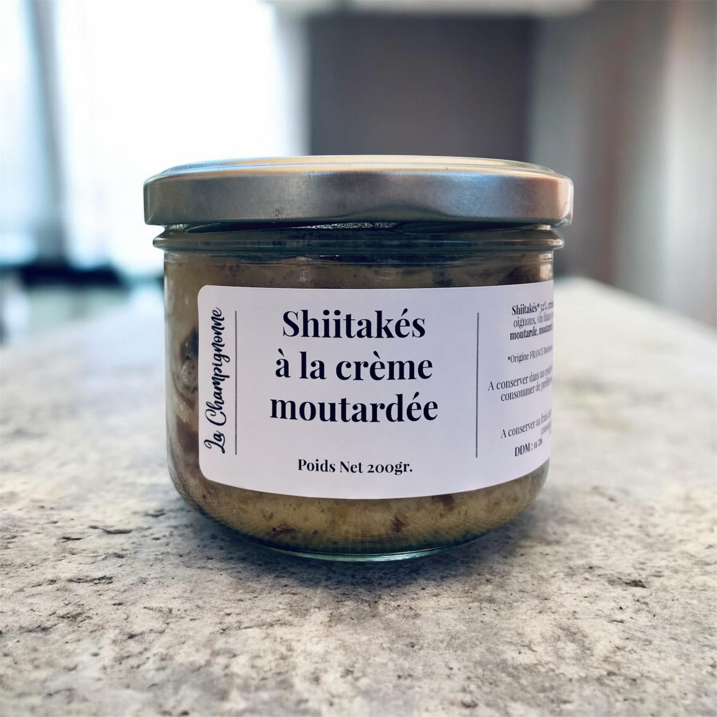 Bocal en verre de shiitakés à la crème moutardée posé sur un plan de travail.